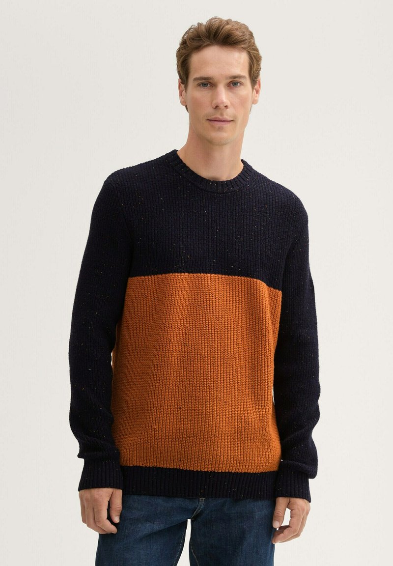 Gebreid sweater met een marineblauwe bovenkant en een oranje onderkant, met een geribbelde textuur en een ronde halslijn.