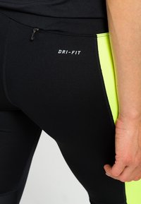 Leggings neri Dri-FIT con pannelli laterali giallo neon, dotati di una tasca con zip e una texture liscia e elastica adatta per l'uso atletico.