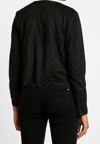 Sort ruskindsjakke med cropped design, der har lange ærmer og afrundet bagkant. Kombineret med sorte tætsiddende jeans.