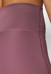 Haut sans bretelles bordeaux en tissu lisse et extensible avec un design sans couture et un éclat subtil. Comprend un détail de couture contrasté.