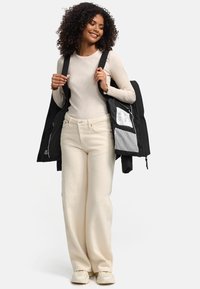 Black puffer jacket held open, worn over a light beige long-sleeve shirt. White wide-leg pants and beige sneakers complete the outfit.