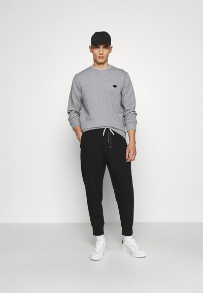 Grijze sweatshirt met ronde hals en klein logo, gecombineerd met zwarte joggerbroek met elastische tailleband en witte sneakers.