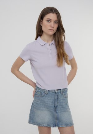 Polo shirt di un leggero viola con colletto classico e pattina con bottoni, abbinato a una mini gonna in denim blu con una texture sfumata.
