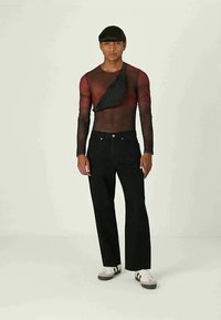 Mustat farkut, joissa on leveä lahje; läpinäkyvä punainen pitkähihaisen verkkopaita mustan ristiin kannettavan laukun kanssa; sileä rakenne ja istuva muotoilu.