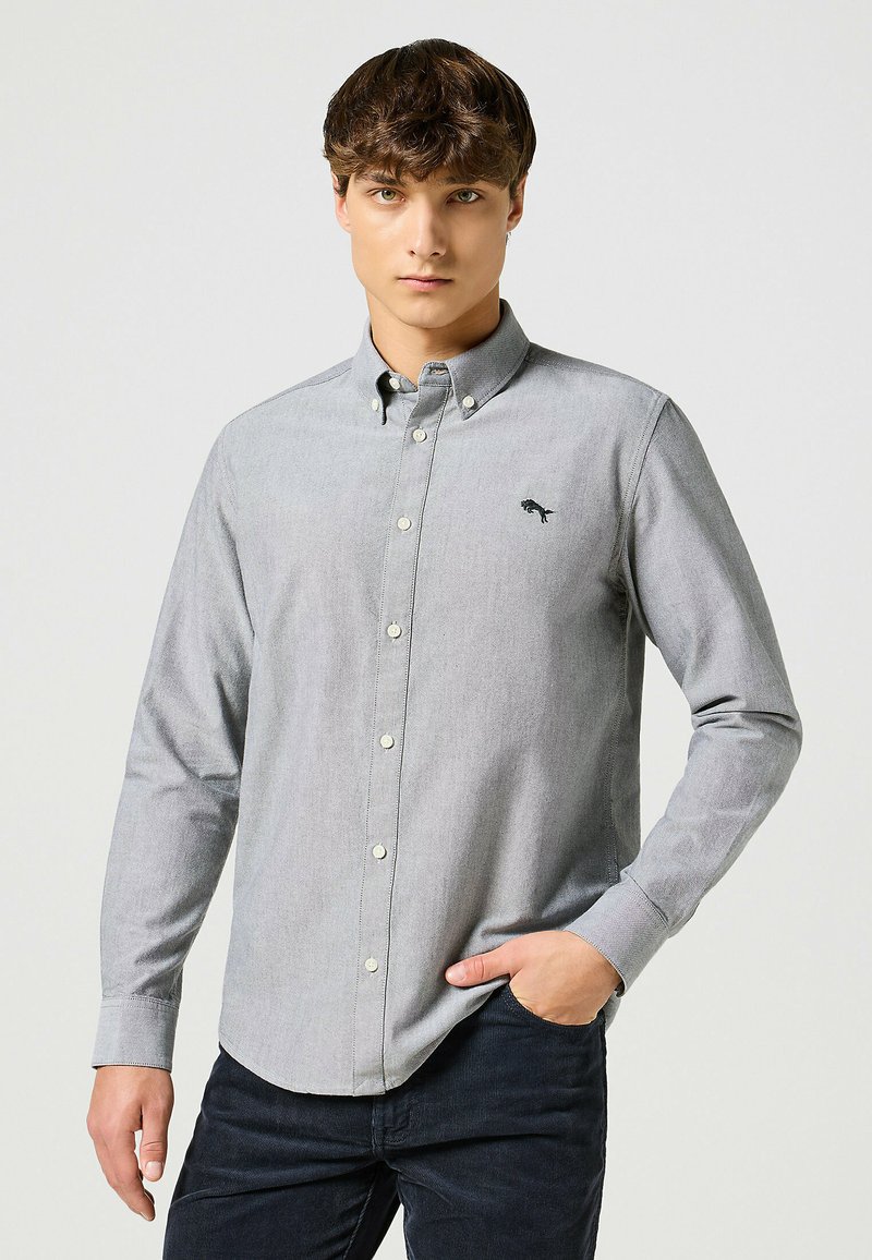 Camisa gris de botones hecha de una mezcla de algodón que presenta un pequeño logo en el pecho, mangas largas y un cuello clásico.