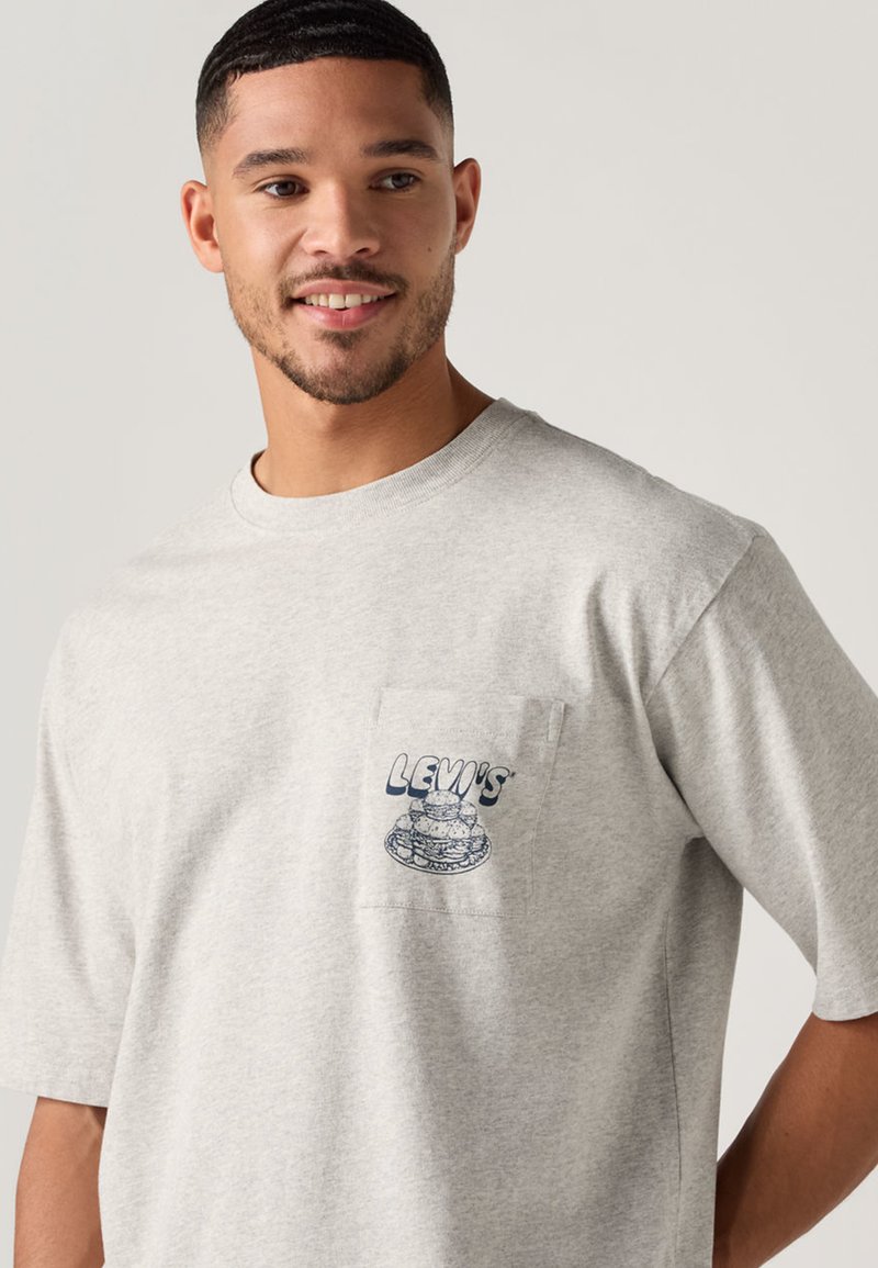 Graues Baumwoll-T-Shirt mit einer Brusttasche, auf der das blaue "LEVI'S"-Logo und eine Illustration abgebildet sind. Kurzärmlig, klassischer Rundhalsausschnitt, entspannte Passform.