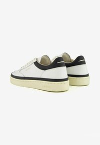 Sneaker in pelle bianca con tallone nero, punta rotonda e suola crema. Presentano cuciture minime e un marchio dorato sul lato.