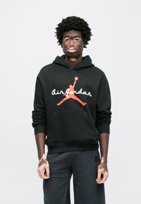 Μαύρο φούτερ με κουκούλα με λογότυπο και σιλουέτα "Air Jordan" σε λευκό και πορτοκαλί χρώμα. Διαθέτει εμπρόσθια τσέπη-κουκούλα και ριμπ μανσέτες. Φορεμένο με σκουρόχρωμο παντελόνι.