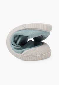 Zapato de tela azul claro con suela de goma blanca texturizada, doblado para mostrar el diseño y los materiales. Punta redondeada y tacón plano.