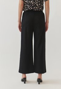Zwarte wijde broek met een zachte textuur, voorzien van een elastische tailleband. Draag een top met korte mouwen en stippen. Hoge hakken zijn zichtbaar.