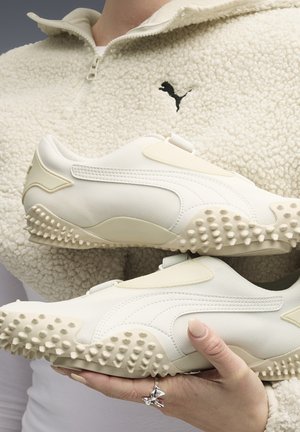 Weiße Sportschuhe bestehen aus einer Kombination aus strukturiertem Mesh und glattem Material, mit einer genoppten Sohle und minimalistischen Designelementen.