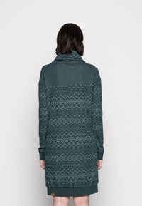 Langarmkleid in dunkeltürkis mit einem Schalkragen. Verfügt über einen gemusterten Mittelteil mit weißen geometrischen Formen und einem einfarbigen Oberteil. Hergestellt aus weichem Stoff.