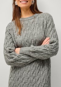 Pull en maille grise avec des poignets et un ourlet côtelés, fabriqué dans un matériau doux et texturé. Doté d'un col rond et d'une coupe décontractée.