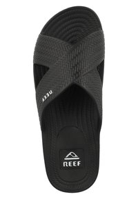 Musta rantapohja, jossa on kudotut ristrapsut, ja sivussa "REEF"-logo sekä teksturoitu pohja, joka tarjoaa pitoa ja mukavuutta.