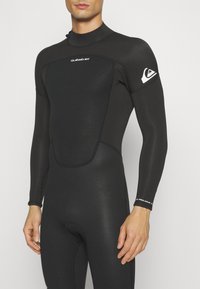 Czarny pianka neoprenowa z długimi rękawami, gładka tekstura, z logo Quiksilver na ramieniu oraz kontrastowymi białymi szwami na mankietach.