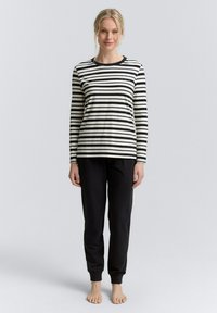 Gestreiftes langärmliges Oberteil in Schwarz und Weiß mit rundem Ausschnitt, kombiniert mit schwarzen tapered Hosen, die an den Knöcheln umgeschlagen sind und aus weichem Stoff bestehen.