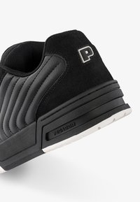 Black suede sneaker with quilted detailing, rubber sole, and a prominent 'P' logo on the heel. Features a textured black and white design.