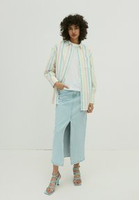 Gestreepte button-up shirt in pastelkleuren, gelaagd over een witte top, gecombineerd met een lichtblauwe denim rok met een split aan de voorkant en blauwe strappy hakken.