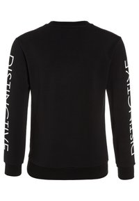 Svart sweatshirt med långa ärmar, med vit text "DISTINCTIVE" på vänster ärm. Gjord av mjukt, texturerat tyg med ribbat nackband.