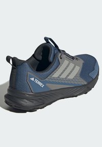 Marineblå trail sko med en tekstureret overdel, grå accenter, tre-stribe logo og en robust sort ydersål designet til holdbarhed og greb.