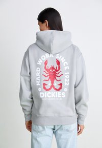 Grå huvtröja med en stor röd krabbgrafik på baksidan, med texten "HARD WORK SINCE 1922" och "DICKIES" i vitt.