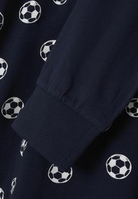 Tessuto blu navy con motivi ripetuti di palloni da calcio bianchi; presenta un polsino con texture arricciata. Materiale di cotone morbido.