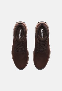 Zapatos de senderismo de cuero marrón con suelas de goma negras, cordones redondos y un logo de Timberland en la plantilla. Apto para uso al aire libre.