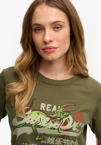 Olijfgroene katoenen t-shirt met een kleurrijke drakenafbeelding met strass-accenten, ronde halslijn en korte mouwen.