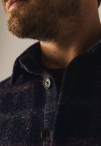 Wollen button-up shirt in een donker marineblauwe kleur met bordeauxkleurige accenten, een klassieke kraag en een zilveren knop met een bloemmotief.