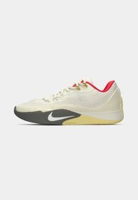 Nike atletiksko med en lys beige mesh-overdel, grå gummisål, gule accenter og en rød polstret krave med gyldne snørehuller.