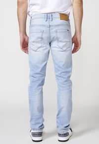 Jeans de denim azul claro con corte ajustado, con bolsillos traseros y una etiqueta de cuero marrón en la cinturilla. Combinados con zapatillas blancas y negras.