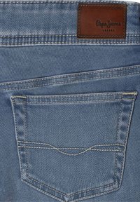 Plava traper tkanina s stražnjim džepom i žutim šavovima. Ima smeđu kožnu oznaku s utisnutim tekstom "Pepe Jeans London".
