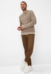 Brown knit sweater with a round neckline and ribbed cuffs, paired with slim-fit brown pants and white sneakers, on a neutral background.