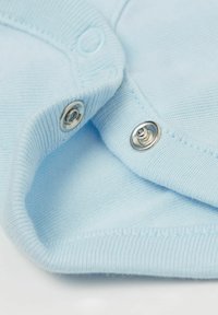 Jasnoniebieska bawełniana tkanina o miękkiej fakturze, z metalowymi zatrzaskami i prążkowanym wykończeniem. Widoczne detale stębnowania.