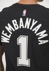 Schwarzes Basketballtrikot mit "WEMBANYAMA" in fetten weißen Buchstaben und der Nummer "1" im Punktmuster, akzentuiert mit einem kleinen NBA-Logo.