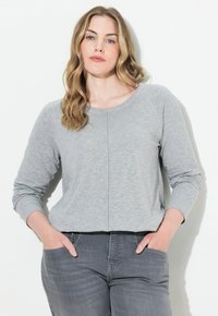 Grijze langemouwen top met een ronde halslijn, zachte textuur, relaxed fit en een centrale naden detail; gecombineerd met grijze jeans.