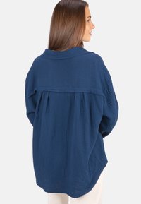 Marineblaues Langarmhemd aus strukturiertem Stoff, mit kragengeschnittenem Ausschnitt, Falten auf der Rückseite und entspannter Passform.