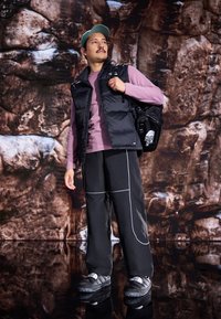 Musta puhvivest, jonka päällä on vaaleanlila pitkähihaista paitaa, yhdistettynä löysiin mustiin housuihin, joissa on valkoiset saumat. Asusteina musta reppu ja teal-värinen hilkka.