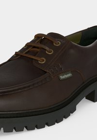 Chaussure à lacets Barbour en cuir brun foncé avec détails cousus et semelle épaisse noire à crampons sur fond clair.