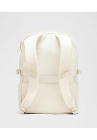 Mochila de color crema hecha de tela suave, con correas ajustables acolchadas, un asa superior reforzada y cierre de cremallera con bolsillos laterales.