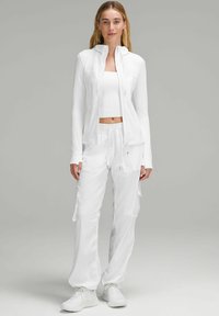 Tenue de sport blanche composée d'une veste ajustée à manches longues, d'un crop top et d'un pantalon cargo, le tout en tissu lisse et léger.