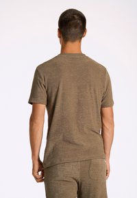 T-shirt leggero, a maniche corte, di colore marrone, realizzato in tessuto testurizzato, con un semplice scollo a girocollo e una vestibilità rilassata, indossato con pantaloni abbinati.