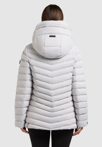 Světle šedá péřová bunda s chevronovým vzorem, velkou kapucí a střih na míru. Má hladkou texturu a jemné logo na zadní straně.