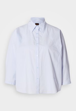 Jasnoniebieska koszula z kołnierzykiem, zapinana na guziki, z rękawami raglanowymi i gładką, odporna na zagniecenia tkaniną. Na dole delikatne hafty.