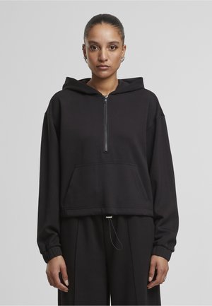 Sort cropped hoodie i blødt materiale, med halv-lynlås foran, forlommer og snøre i kanten. Oversized pasform med lange ærmer.