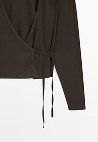 Mørkebrun omslagstop med lange ærmer, der har en dyb V-hals og en bindedetalje på den ene side. Fremstillet af blødt, fleksibelt stof.