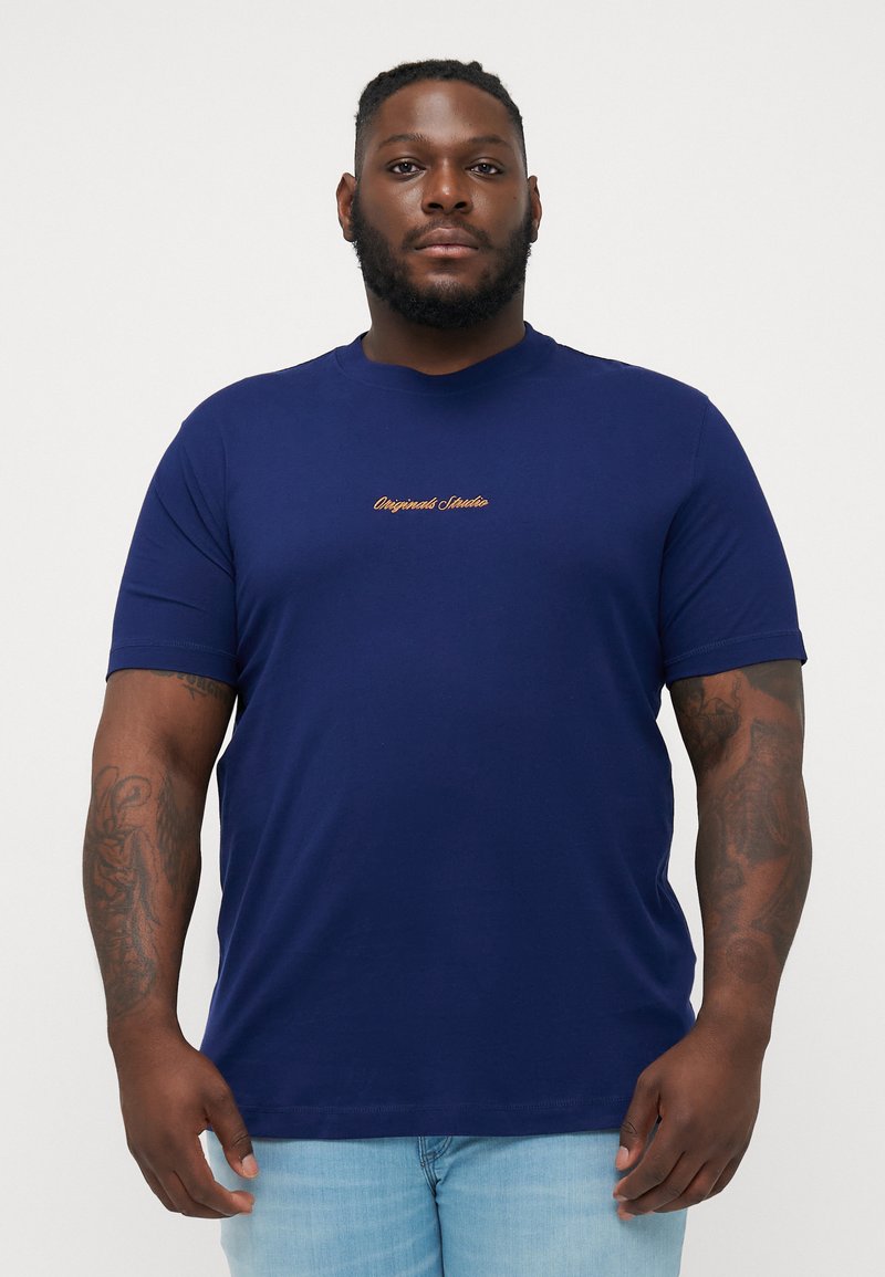 Camiseta de manga corta azul marino hecha de una tela suave, con "Originals Studio" bordado en contraste en el pecho.