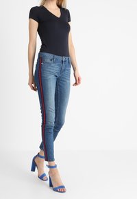 Camiseta de pico en navy combinada con jeans ajustados azules con rayas laterales rojas y sandalias de tacón azules con correas al tobillo.