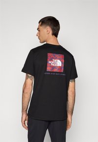Tricou negru din bumbac, cu un logo grafic colorat pe spate, având textul "THE NORTH FACE" și "NEVER STOP EXPLORING" sub el.