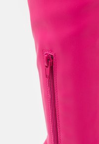 Kirkkaan pinkki polven yläpuolelle ulottuva saapas, valmistettu sileästä synteettisestä materiaalista, jossa on sivuvetoketju ja hienovarainen ompelukuvio.